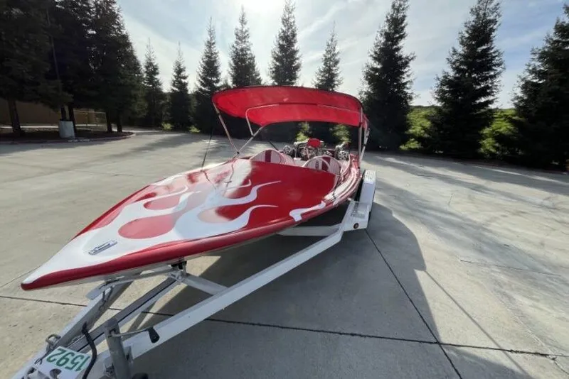 Slide: The Image of Red 1975 Weirdt Maverick speedboat with flame design on trailer, surrounded by trees. - 8