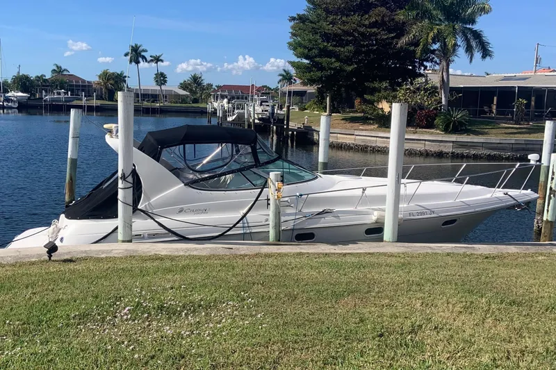 Slide: The Image of 1998 Cruisers 3375 Esprit yacht docked by a serene waterfront with palm trees. - 2