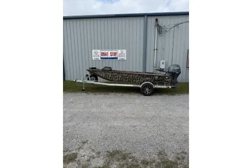 The Image of 2026 Avid 16 Commander boat with camouflage design, parked outside a metal building. - 0