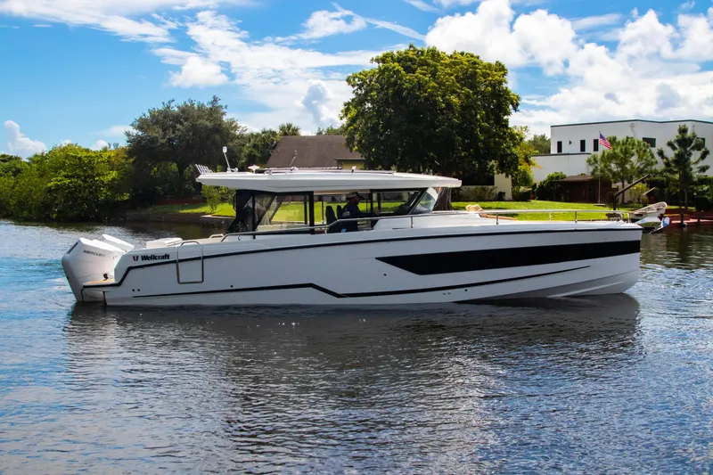 Slide: The Image of 2025 Wellcraft 38 Explorer boat cruising on a sunny day, surrounded by lush greenery. - 8