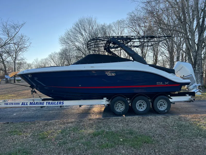 Slide: The Image of 2024 Sea Ray SLX 260 Outboard on trailer, blue hull, cloudy sky. - 2