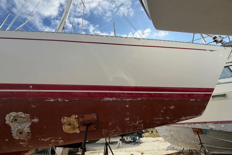Slide: The Image of 1983 Morgan Catilina sailboat hull with red stripe, dry docked under blue sky. - 11