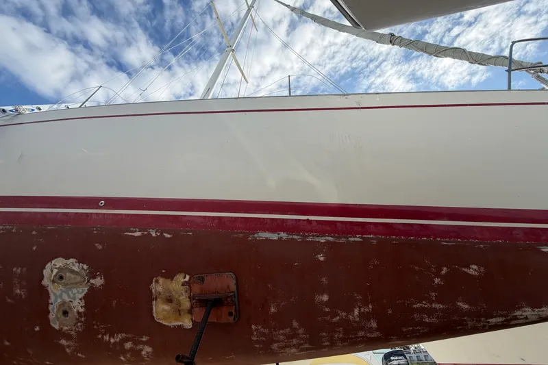 Slide: The Image of 1983 Morgan Catilina sailboat hull with red stripe, under a blue sky with clouds. - 12