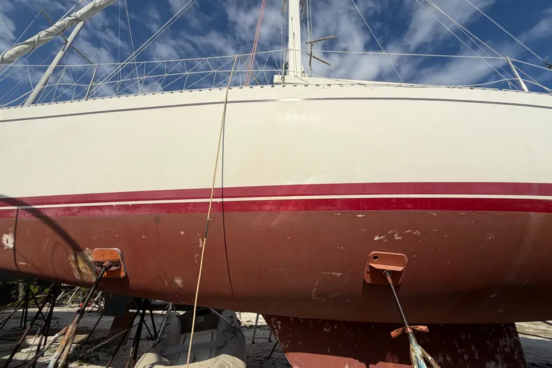 Slide: The Image of 1983 Morgan Catilina sailboat on land, white hull with red stripe, clear sky background. - 3