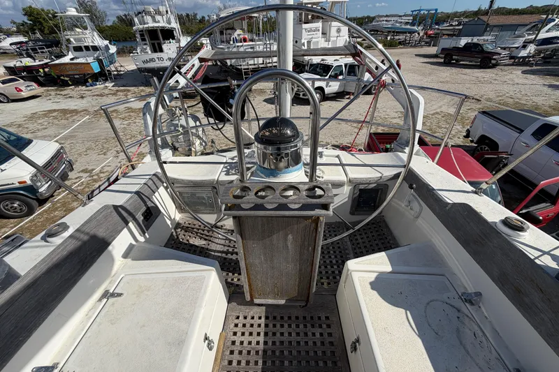 Slide: The Image of 1983 Morgan Catilina sailboat cockpit with steering wheel, docked among various vehicles and boats. - 58