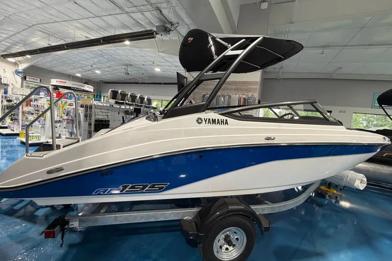 The Image of 2026 Yamaha Boats AR195 in showroom, blue and white design, on trailer. - 0