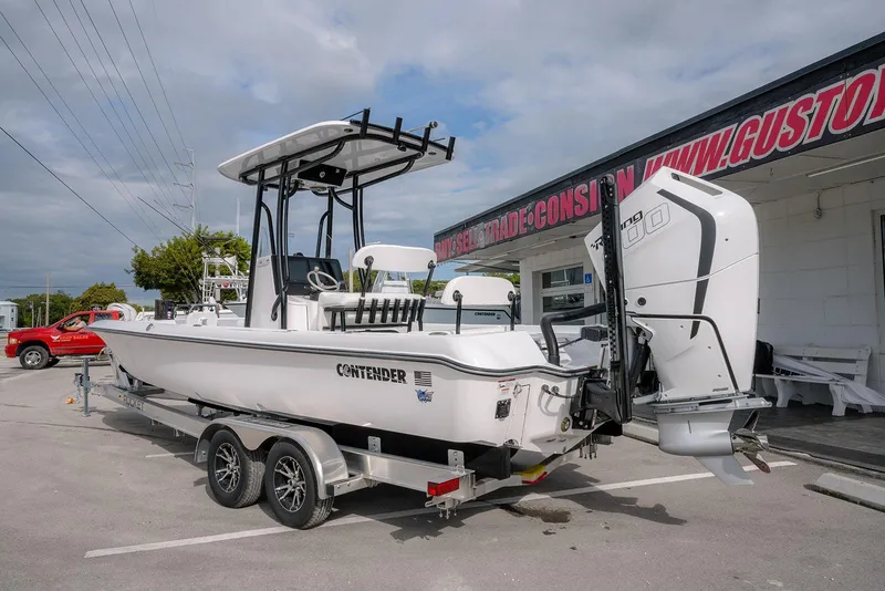 Slide: The Image of 2026 Contender 26 Bay boat on trailer, parked outside dealership under cloudy sky. - 5