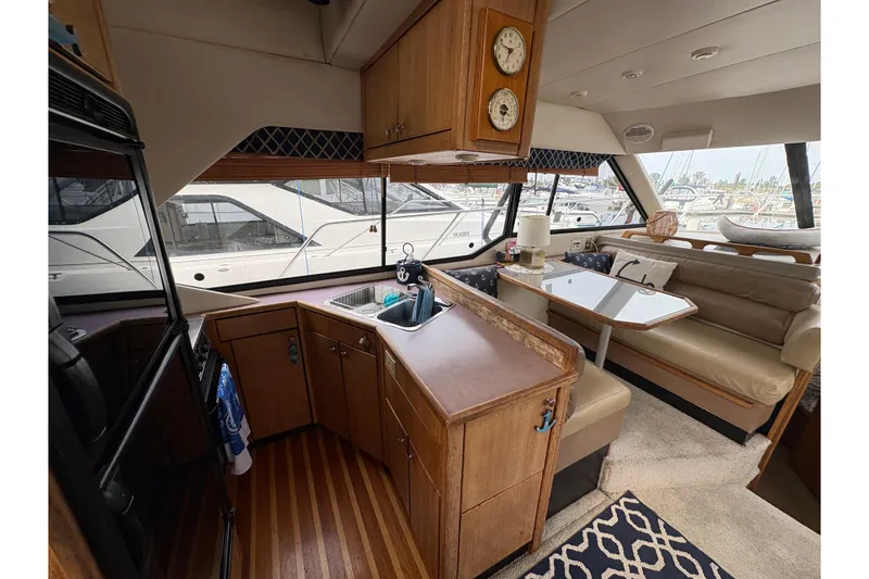Slide: The Image of 1988 Bayliner 3587 Motoryacht interior with kitchen and dining area, featuring wood cabinetry and seating. - 42