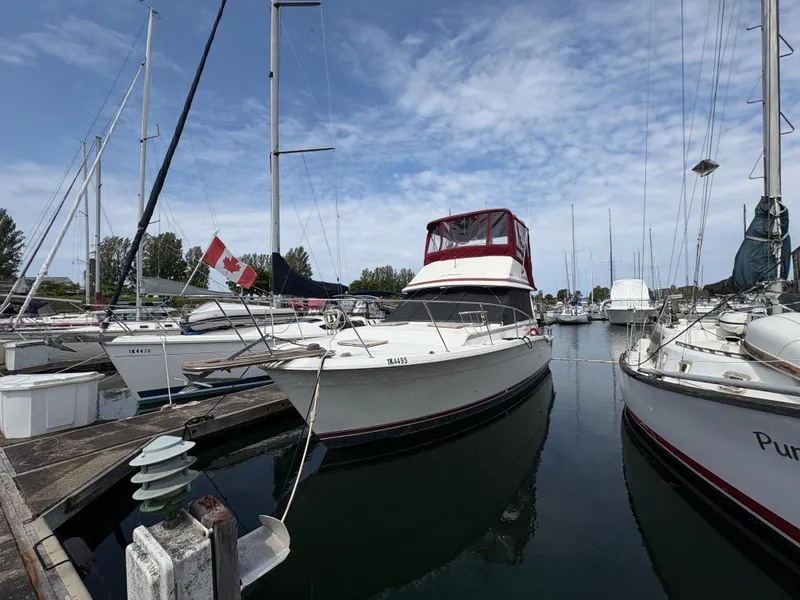 The Image of 1986 Trojan 32 Sedan boat docked in marina with Canadian flag, under blue sky. - 0