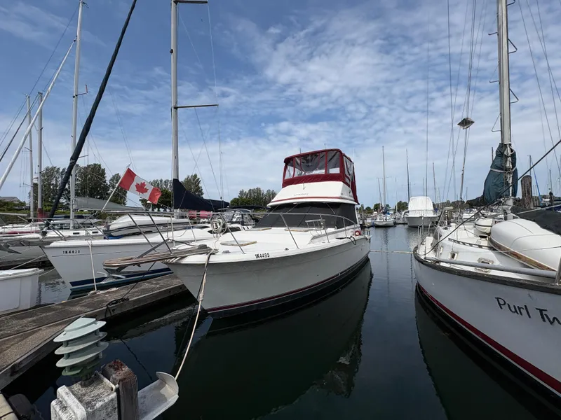 Slide: The Image of 1986 Trojan 32 Sedan docked at marina, surrounded by sailboats, under a partly cloudy sky. - 2