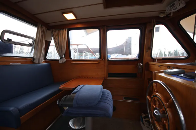 Slide: The Image of 1984 Nauticat 33 interior with wooden helm, blue seating, and large windows. - 11