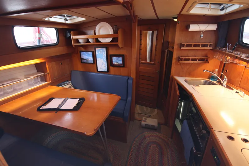 Slide: The Image of 1984 Nauticat 33 yacht interior with cozy dining area, wooden cabinetry, and compact kitchen. - 18