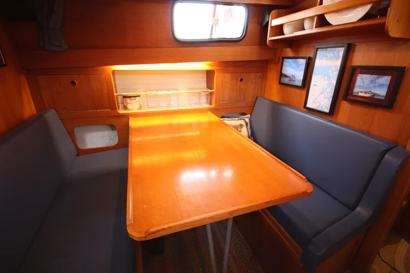 Slide: The Image of Cozy dining area in a 1984 Nauticat 33 sailboat with wooden table and blue seating. - 19