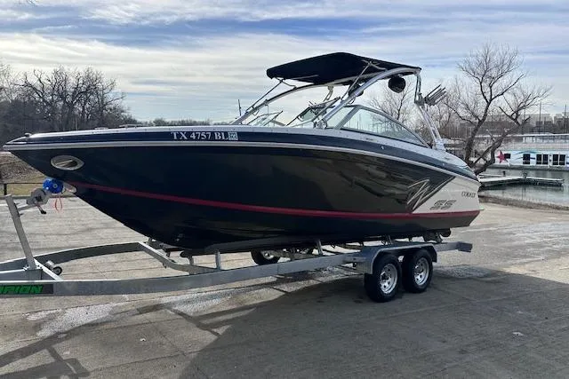 Slide: The Image of 2011 Cobalt 242 WSS boat on trailer, parked near a lake with trees in the background. - 4