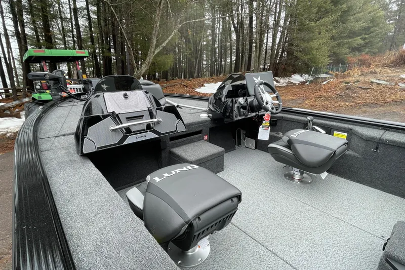 Slide: The Image of 2026 Lund 2075 Pro-V Bass XS boat interior with modern seating and steering, surrounded by forest. - 7