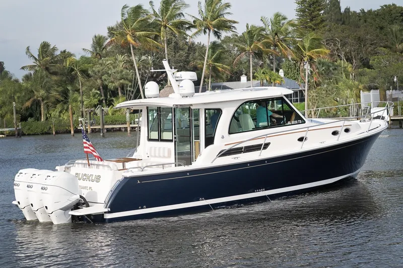 Slide: The Image of 2023 Back Cove 39O boat cruising on a scenic waterway with lush greenery. - 5