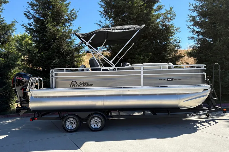 The Image of 2026 Sun Tracker Fishin' Barge 20 DLX pontoon boat on trailer, parked outdoors. - 0