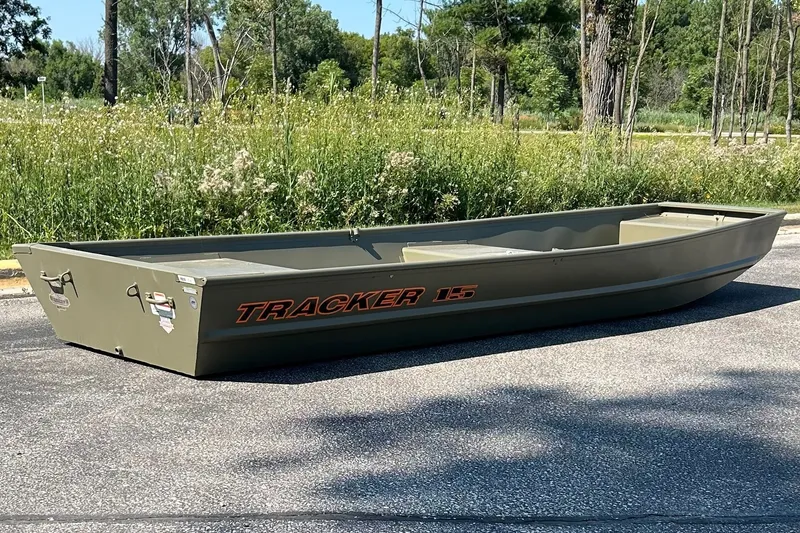 The Image of 2026 Tracker Grizzly 15 Jon boat on pavement, surrounded by greenery. - 0