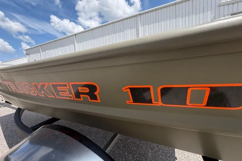Slide: The Image of 2026 Tracker Grizzly 10 Jon boat with bold orange lettering under a blue sky. - 2