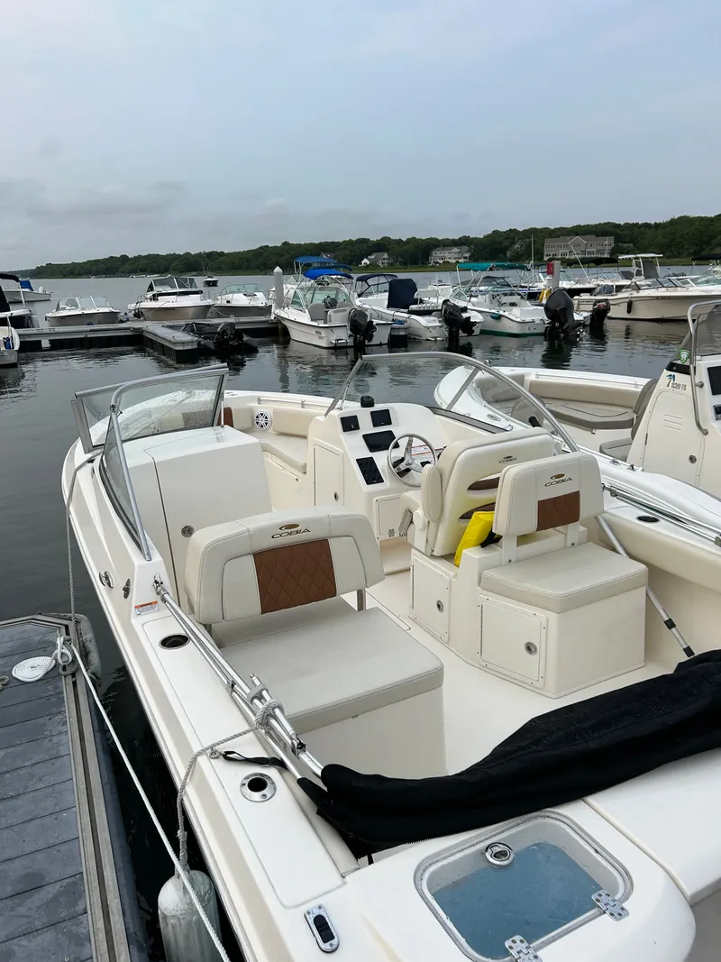 Slide: The Image of 2023 Cobia 220 Dual Console boat docked at marina. - 2