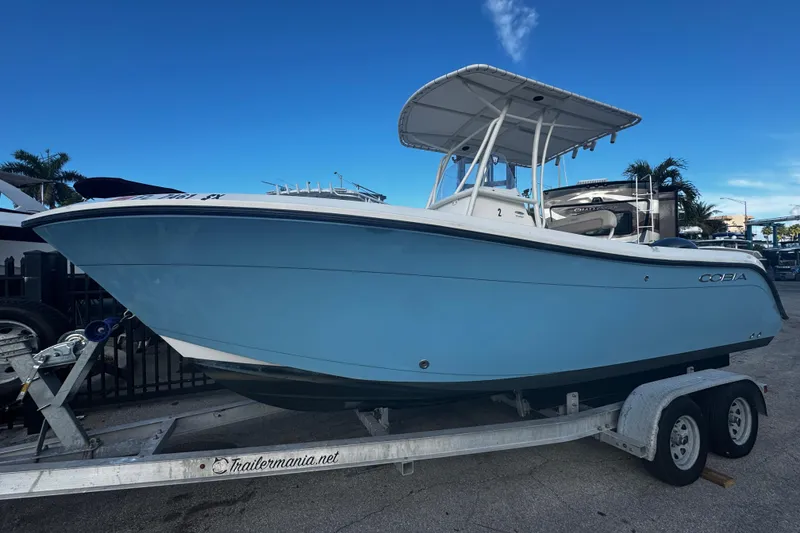 The Image of 2021 Cobia 220 Center Console boat on trailer, blue hull, clear sky background. - 1