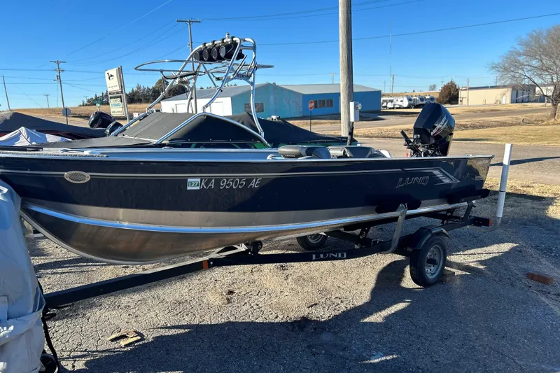 Slide: The Image of 2024 Lund 1600 Fury Tiller boat on trailer, parked outdoors under clear blue sky. - 2
