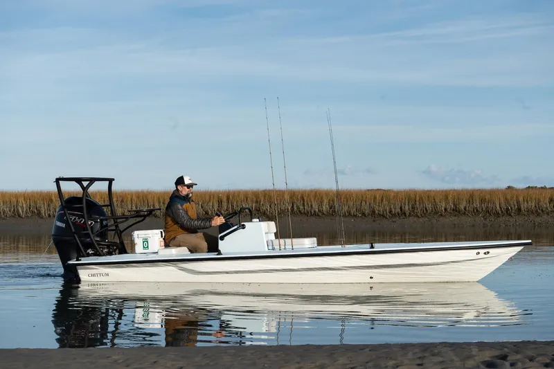 Slide: The Image of 2025 Chittum Skiffs 18 Islamorada boat on calm water, with a person steering. - 4