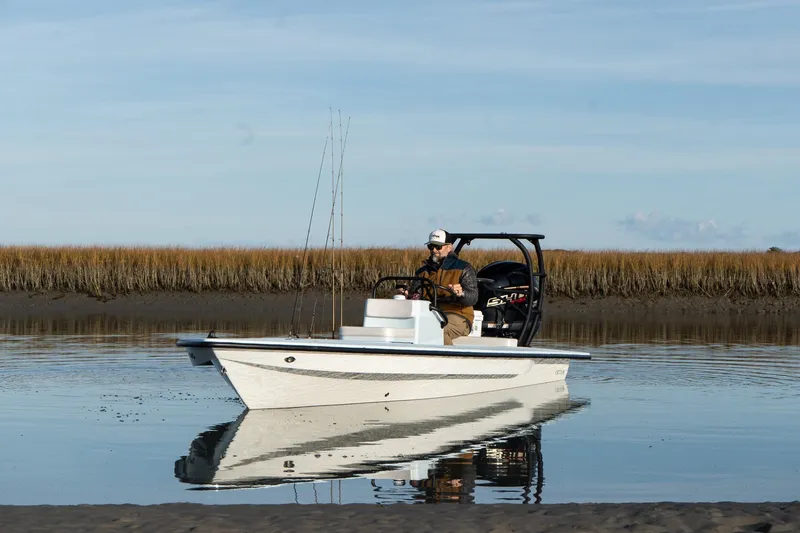 Slide: The Image of 2025 Chittum Skiffs 18 Islamorada boat on calm water, man steering, marshland background. - 7