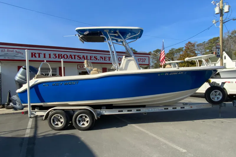 The Image of 2019 Key West 239 FS boat on trailer at dealership, blue hull, sunny day. - 1