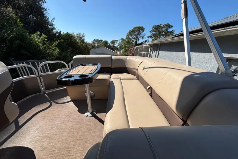 Slide: The Image of 2019 Sun Tracker Party Barge 20 DLX interior with beige seating and table, outdoor setting. - 64