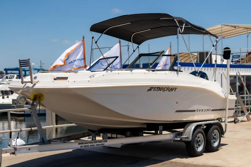 Slide: The Image of 2023 Starcraft SVX 190 OB boat on trailer at marina, featuring sleek design and canopy. - 2