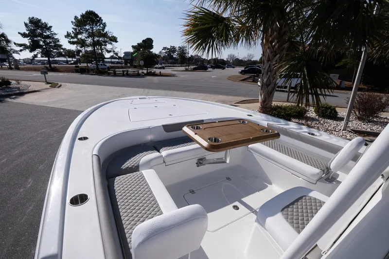 Slide: The Image of 2026 Caymas 28 HB boat interior with seating and table, parked near palm trees. - 14