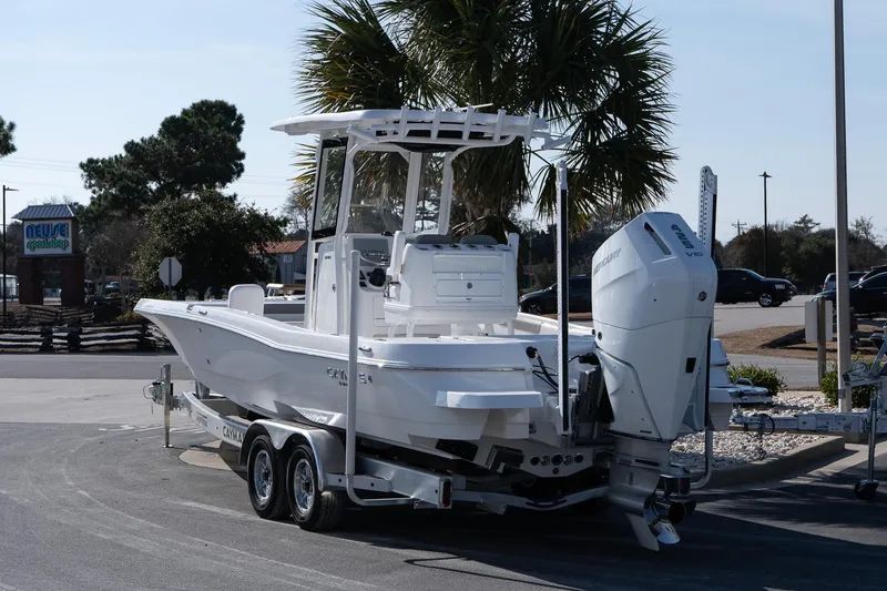 Slide: The Image of 2026 Caymas 28 HB boat on trailer, parked near palm trees and a shop. - 4