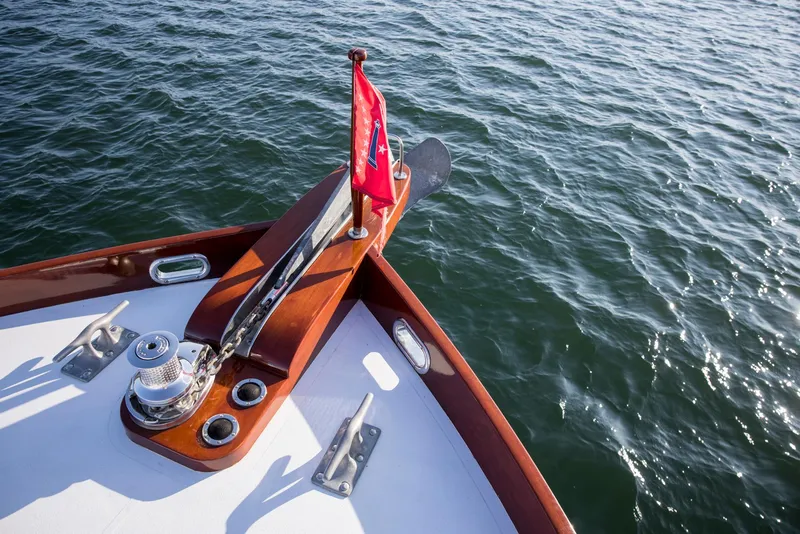 Slide: The Image of Bow of 1964 Huckins Out Islander 56 yacht with red flag on calm water. - 16