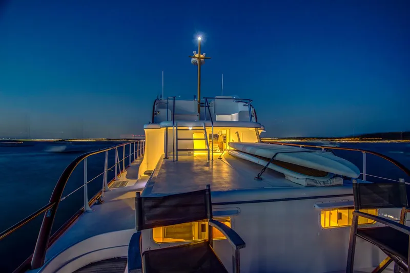 Slide: The Image of 1964 Huckins Out Islander 56 yacht at dusk, illuminated deck, serene water backdrop. - 46