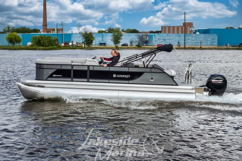 The Image of 2026 Godfrey Sweetwater 2286 SFLX pontoon boat cruising on a river under a cloudy sky. - 1