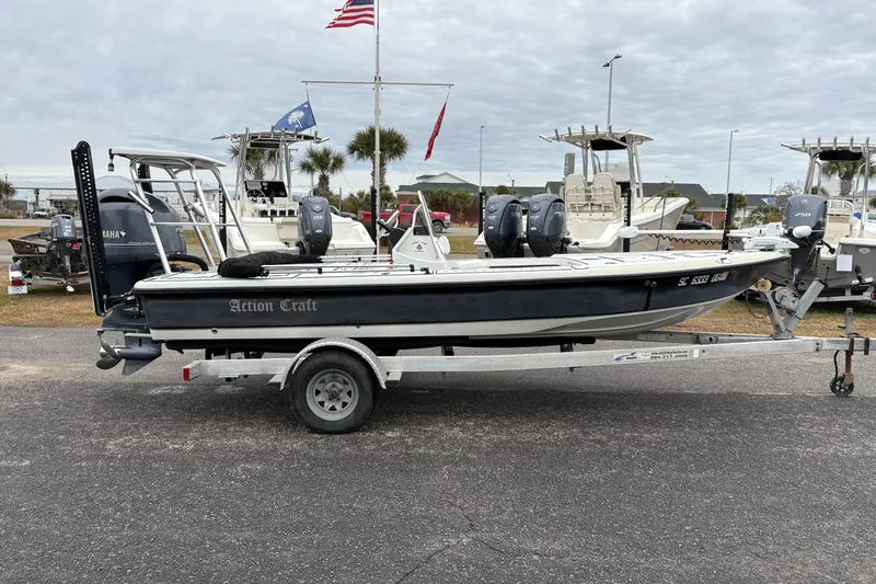 Slide: The Image of 2017 Action Craft Flatsmaster 1820 boat on trailer, parked with other boats in background. - 5