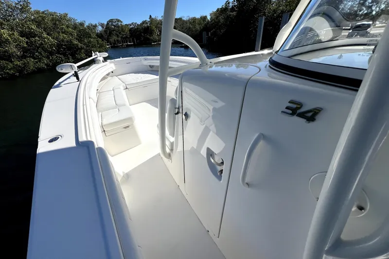 Slide: The Image of 2018 Regulator 34 Center Console boat, white interior, sleek design, docked near lush greenery. - 50