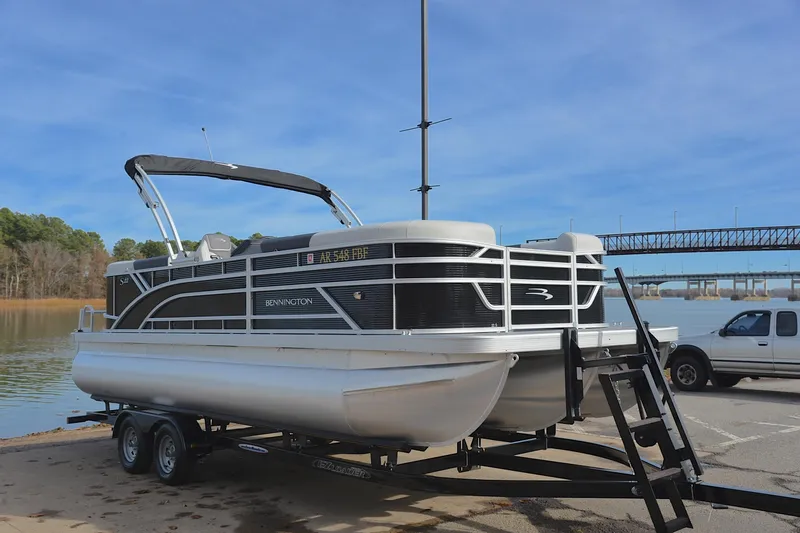 Slide: The Image of 2025 Bennington 22 S pontoon boat on trailer by a lake with bridge in background. - 16
