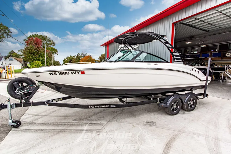 Slide: The Image of 2025 Chaparral 23 SSi boat on trailer outside a garage, under a cloudy sky. - 9
