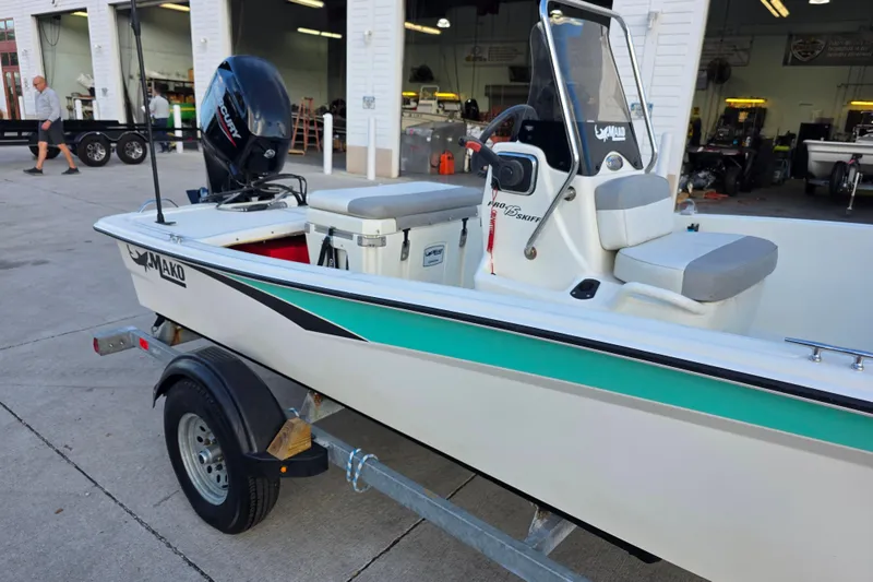Slide: The Image of 2022 Mako Pro Skiff 15 CC boat on trailer, parked outside a workshop. - 2