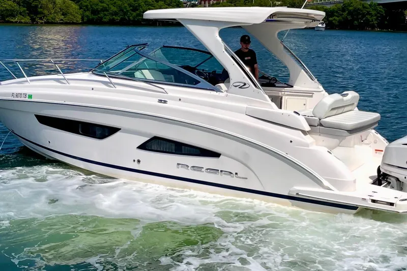 The Image of 2021 Regal 33 XO boat cruising on a sunny day, with lush greenery in the background. - 0