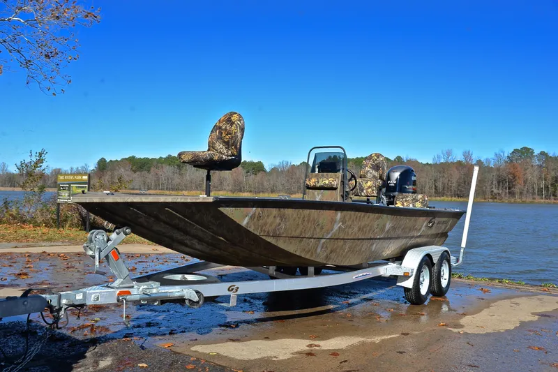 Slide: The Image of 2017 G3 Bay 20 DLX Camo boat on trailer by a lake under clear blue sky. - 10