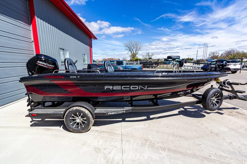 Slide: The Image of 2025 Recon 895 Tiller boat with Mercury engine on trailer, parked outdoors. - 2