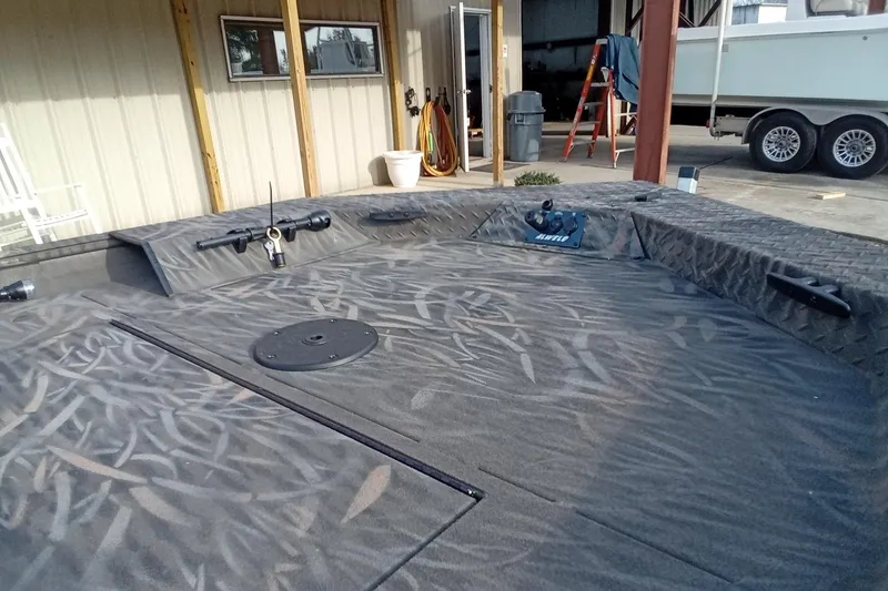 Slide: The Image of 2026 Alweld 1552 Invader boat interior with camo pattern, docked near a workshop. - 8