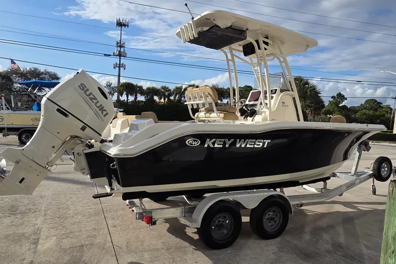Slide: The Image of 2018 Key West 219 FS boat with Suzuki engine on a trailer, parked outdoors. - 2