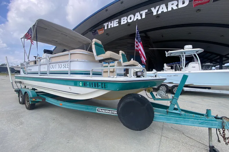 Slide: The Image of 1994 Hurricane FunDeck 226 boat on trailer at The Boat Yard, featuring canopy and American flag. - 10