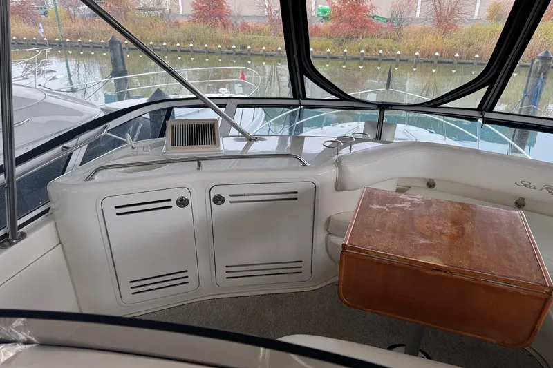 Slide: The Image of 2003 Sea Ray 480 Sedan Bridge interior with seating and wooden table, docked by the water. - 36