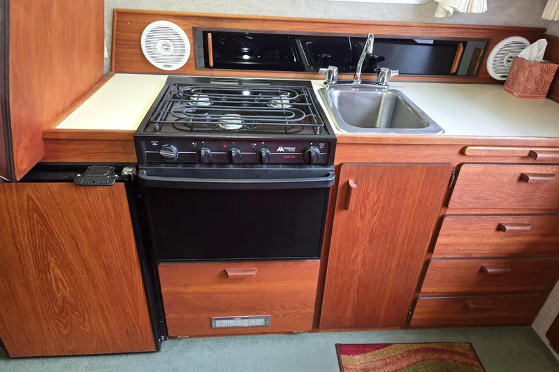 Slide: The Image of 2001 Commander Flybridge Sedan kitchen with stove, sink, and wooden cabinetry. - 72