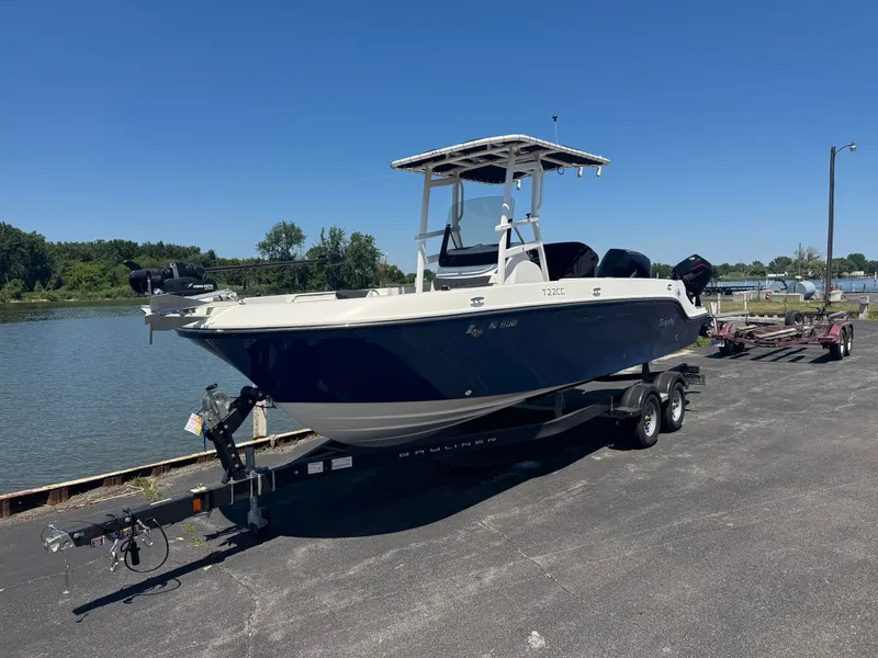 The Image of A 2023 Bayliner Trophy T22CC on a trailer by the water. It features a blue hull design. - 0